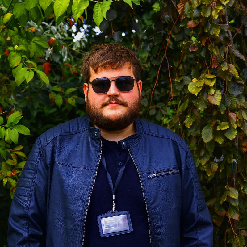 Sam, founder of Scorpion AI Tooling, standing in front of a hedge wearing a navy jacket and a Scorpion AI Tooling lanyard